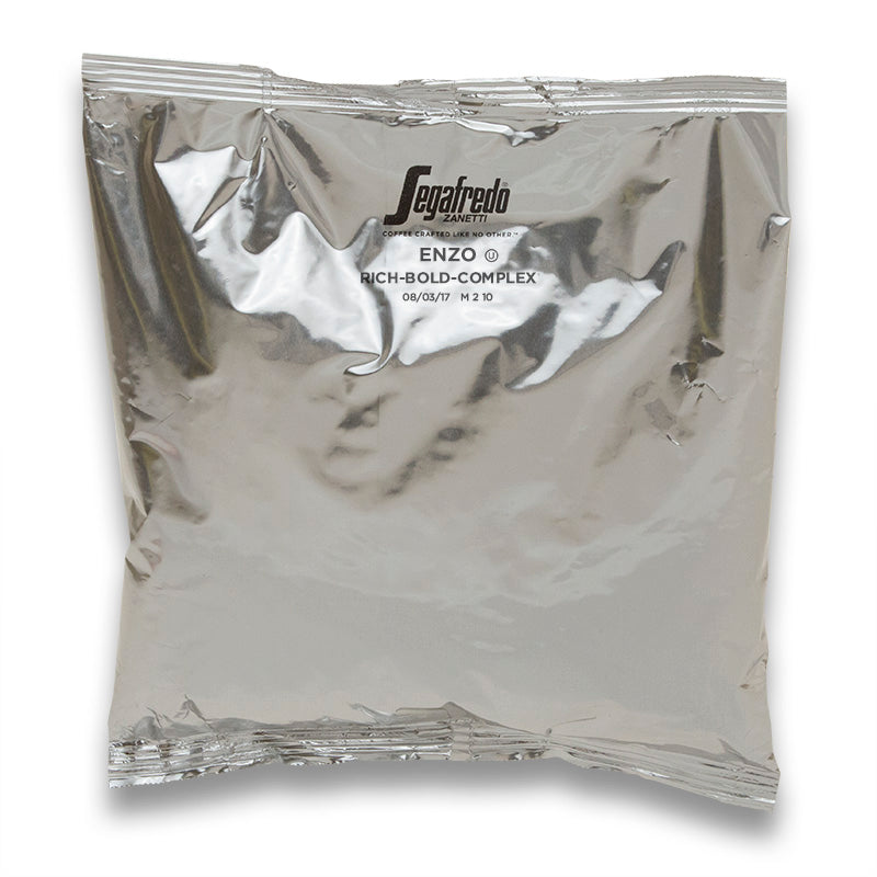 Silver vacuum-sealed coffee bag with the label "Segafredo Zanetti Enzo Dark Roast" describing the coffee as "rich-bold-complex," including a best by date. Contains exclusively Arabica beans.